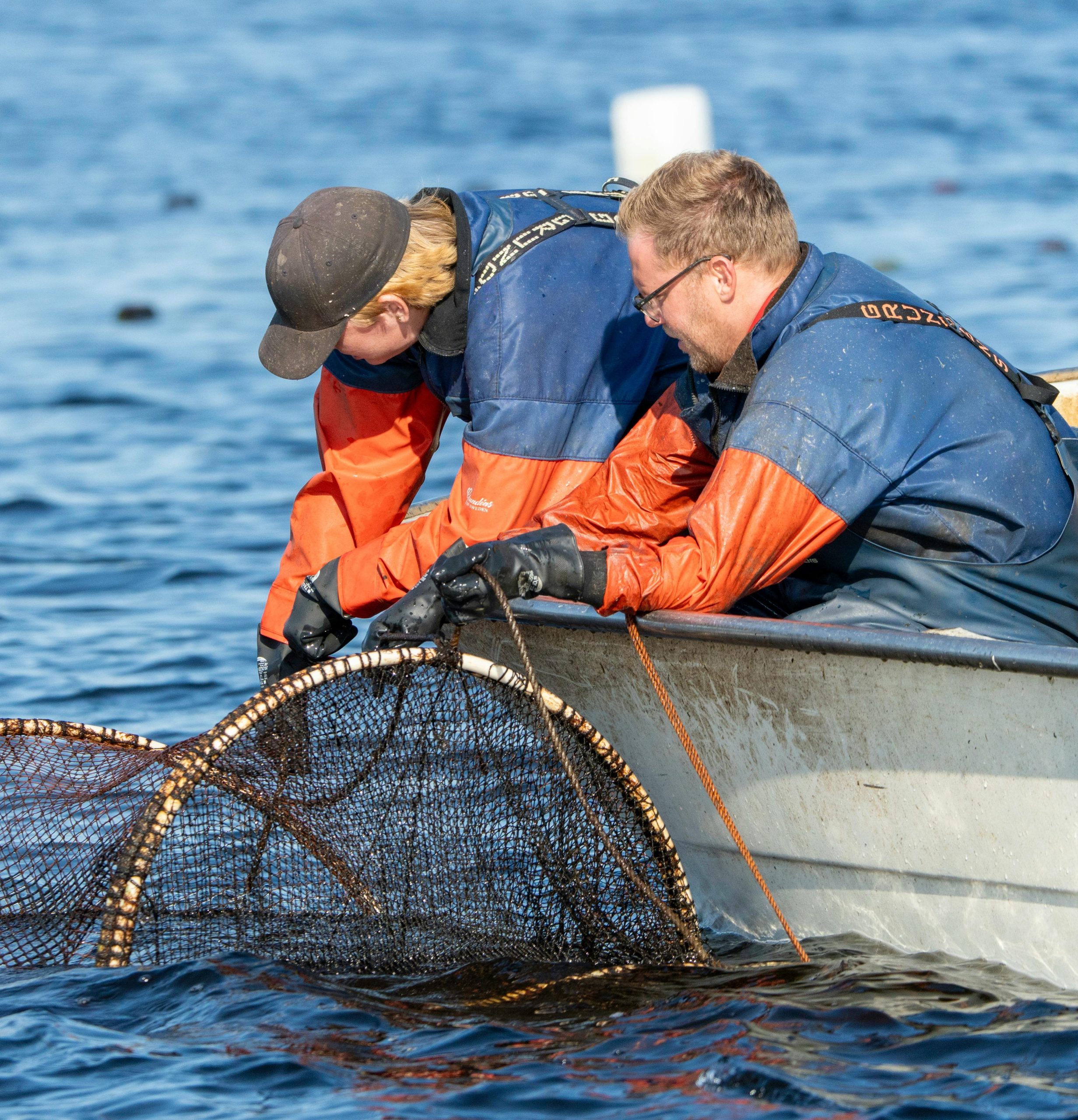 Two fishermen deploying a net from the side of a small boat. Photo by Lorenzo Manera.
